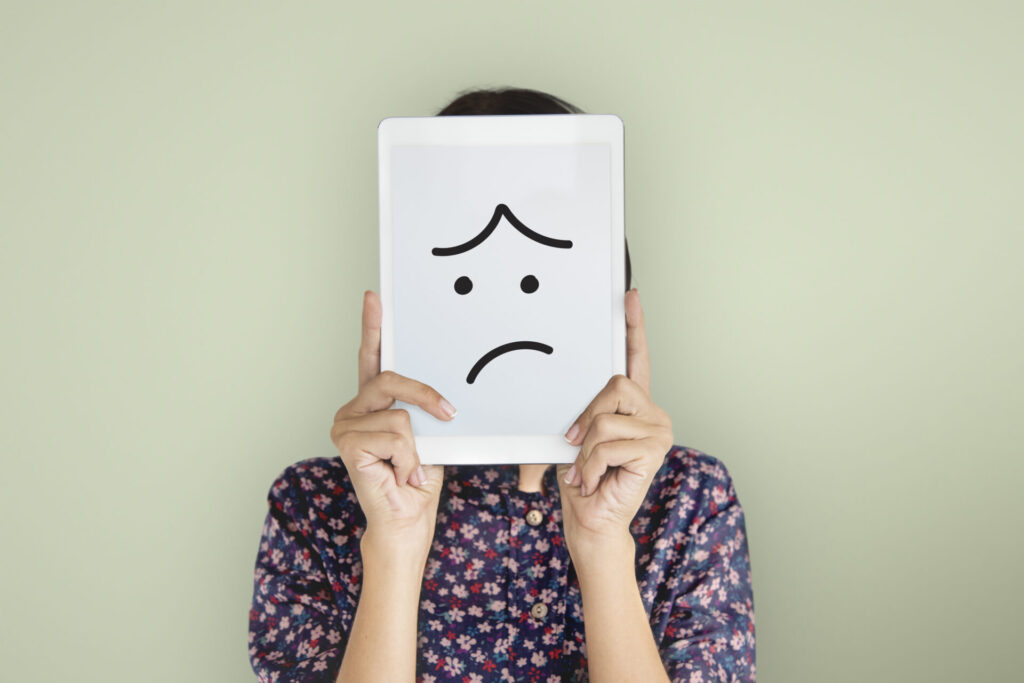 A woman showing sad smiley in a tablet in front of her face